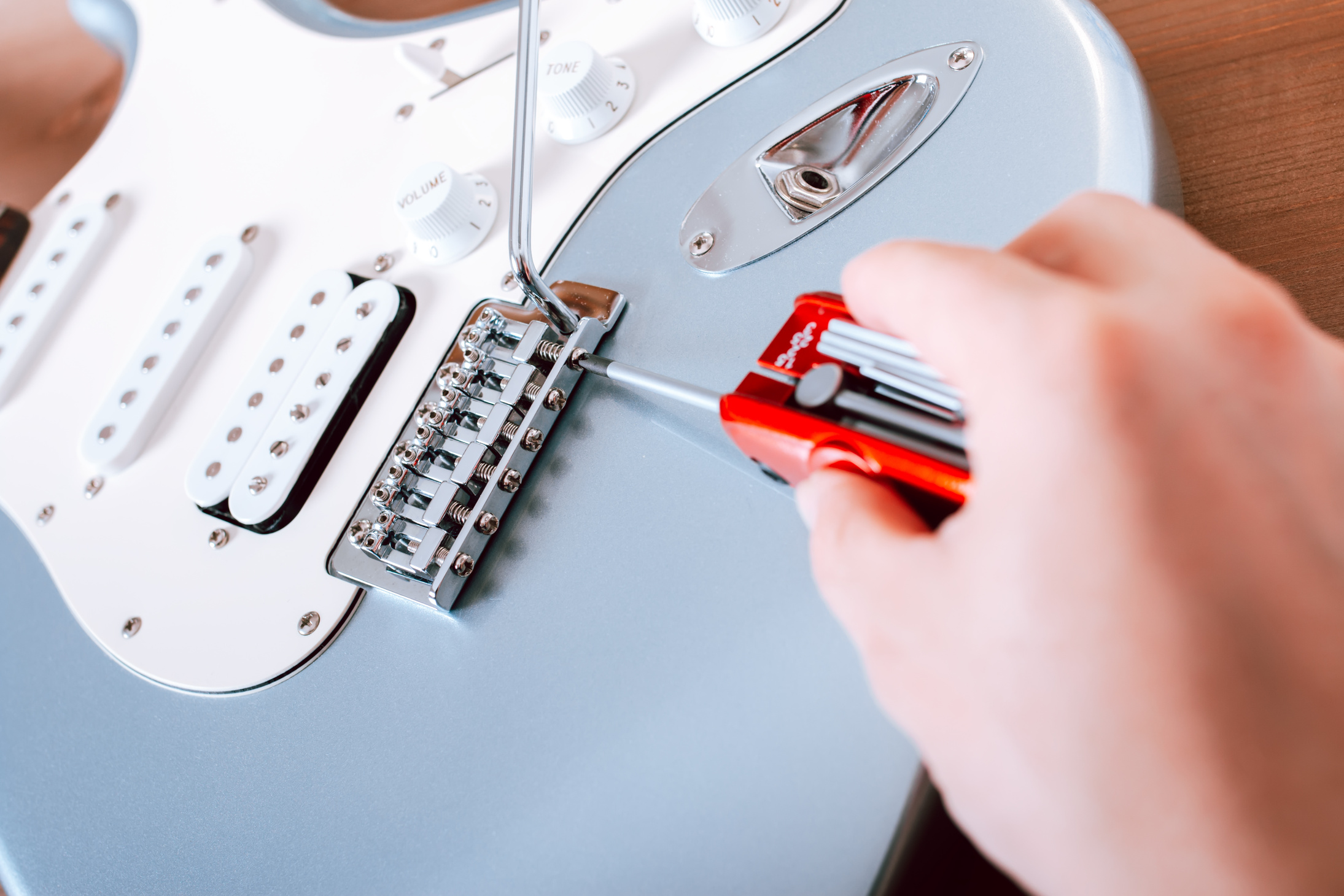 Guitar Master Adjusting Bridge Saddle on Tremolo of Electric Guitar Using Multitool